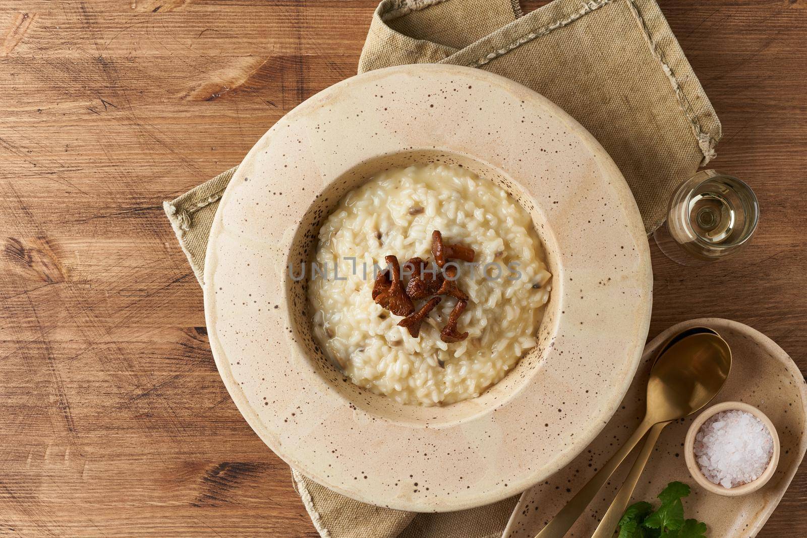 Risoto with chanterelle mushrooms in large plate. Traditional italian dish. Wooden old table, spoons, napkin. Classic hot dish of rice, cheese and wine. Top view, copy space