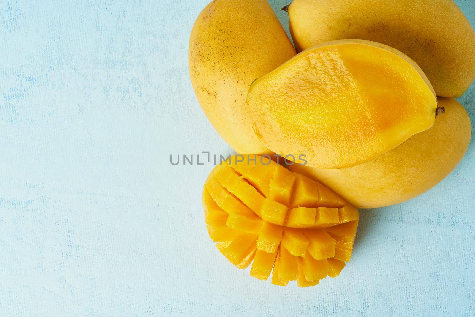 Four whole mango fruits on bright blue table and cut into slices. Large juicy bright ripe yellow fruits on color background, close up, copy space