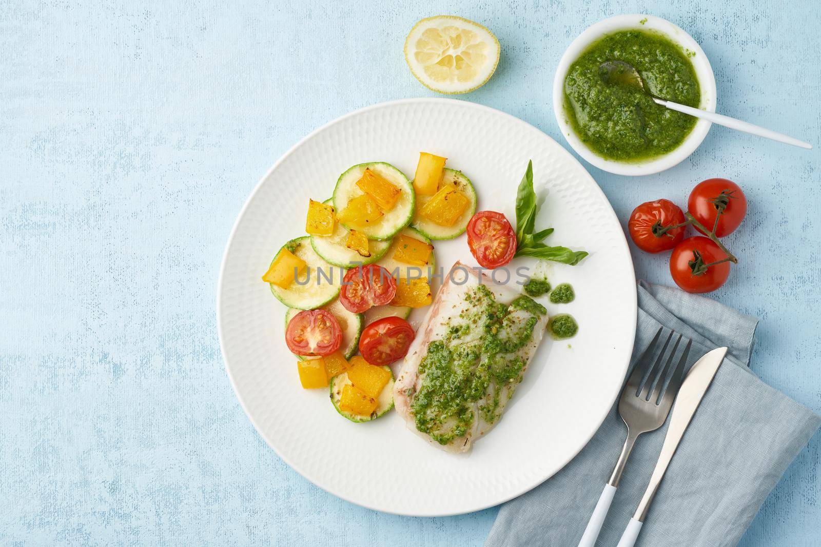 Keto dinner with white fish. Oven baked fillet of cod, pike perch with vegetables and pesto sauce. Healthy diet food, ketogenic paleo diet, Mediterranean cuisine. Blue background. Top view, copy space