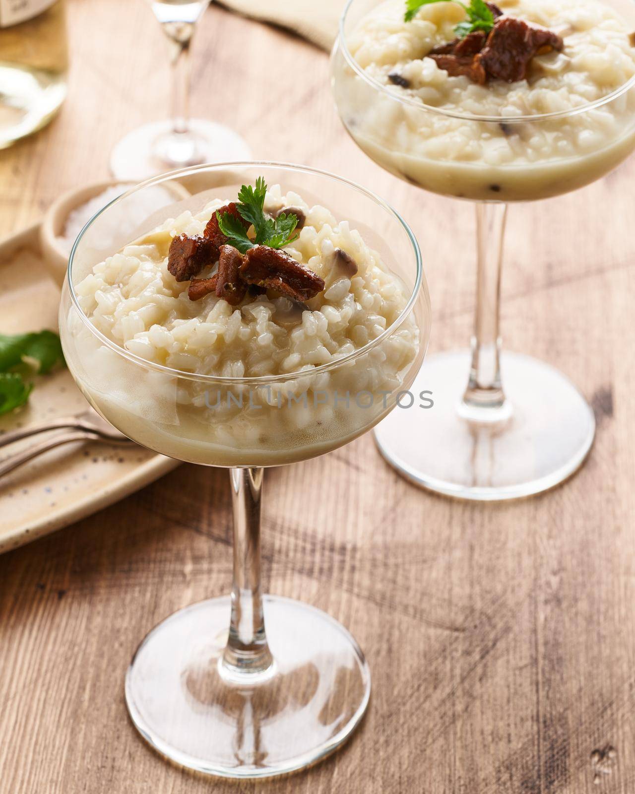 Risotto with mushrooms in wine glass. Unconventional unusual serving. Rice porridge with mushrooms. Wooden old table. Hot dish in glass bowl. Side view, vertical