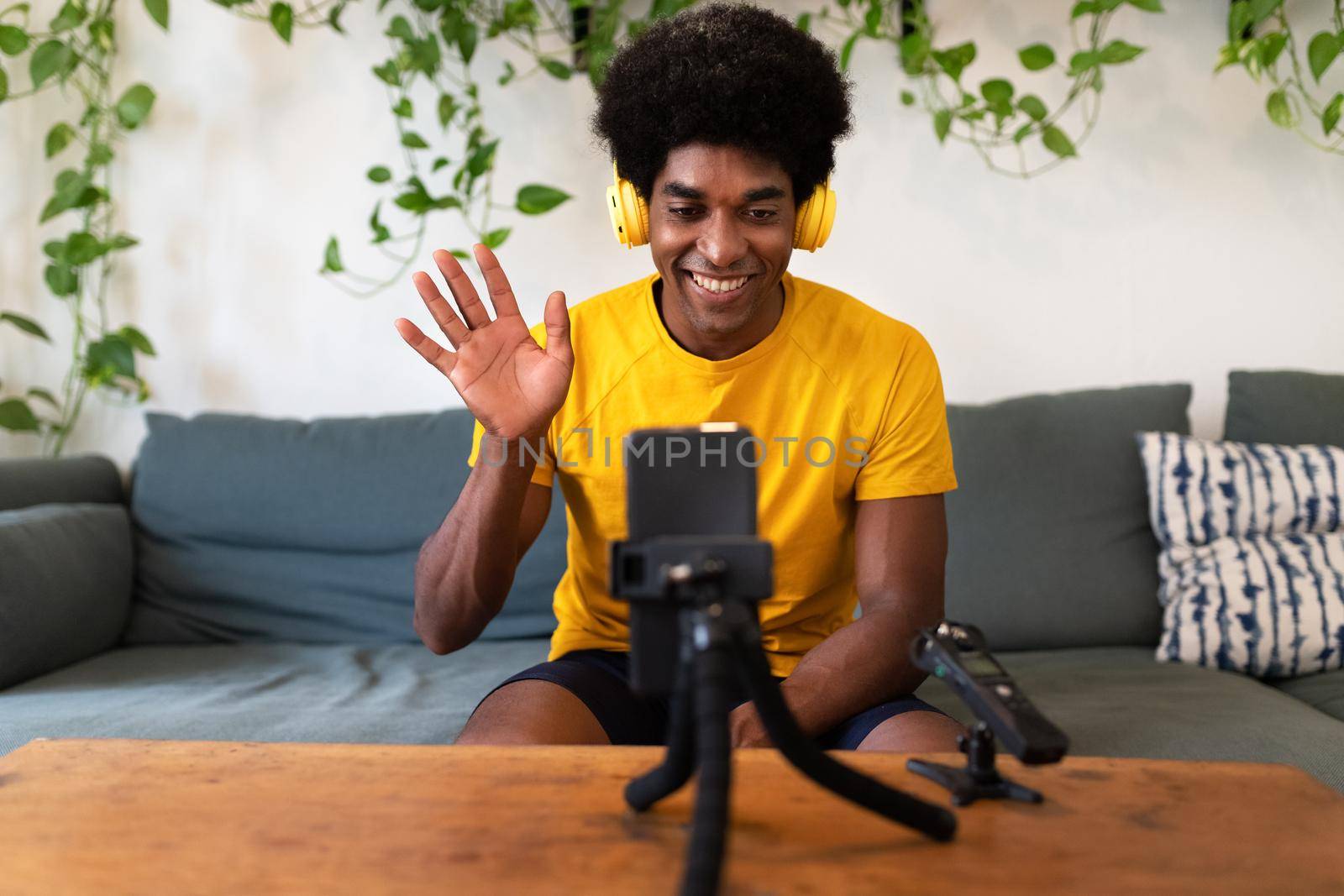 Young african american influencer waving hello to followers. Recording himself for video tutorial with mobile phone. Blogging concept.