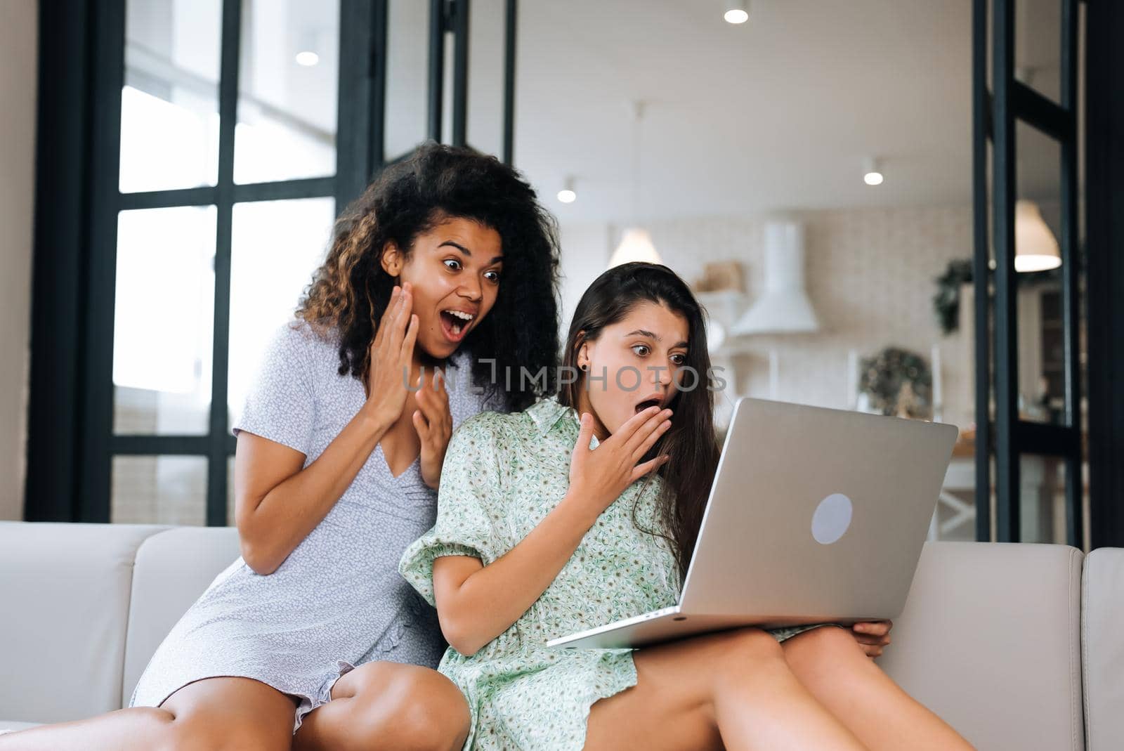 Two beautiful young women relaxing on the living room floor looking at a laptop computer and laughing at something on the screen