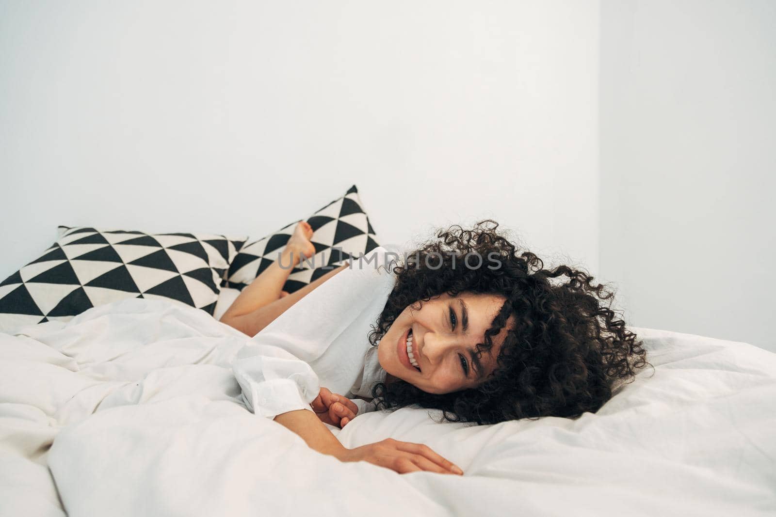 Smiling playful mixed race woman lying on bed looking at camera. Copy space. Lifestyle concept.
