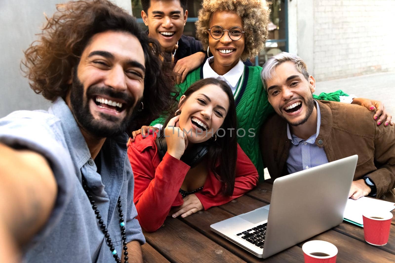 Selfie of multiracial friends looking at camera in a casual business meeting at restaurant terrace outdoors. by Hoverstock