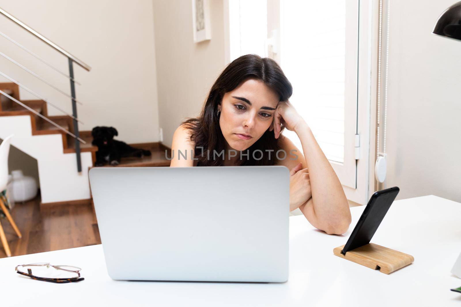 Young caucasian woman bored and frustrated in front of laptop working at home. by Hoverstock