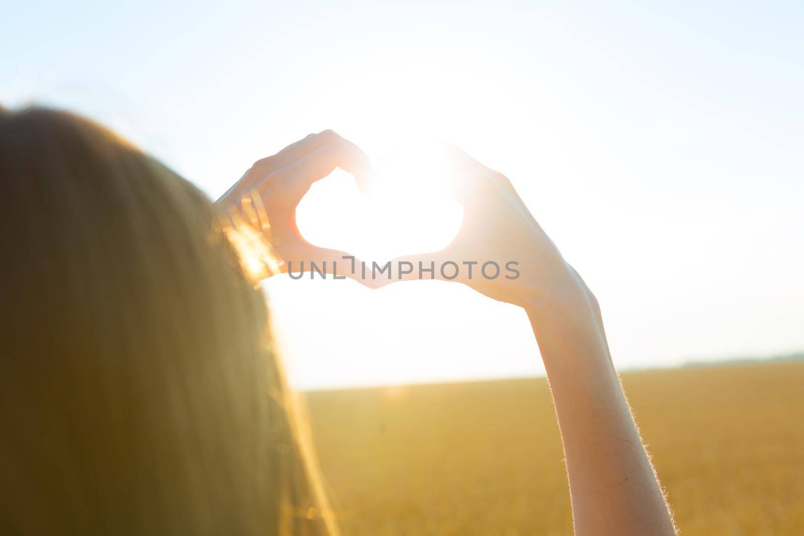 Girl making heart symbol with her hands at sunset on nature background by AlikMulikov