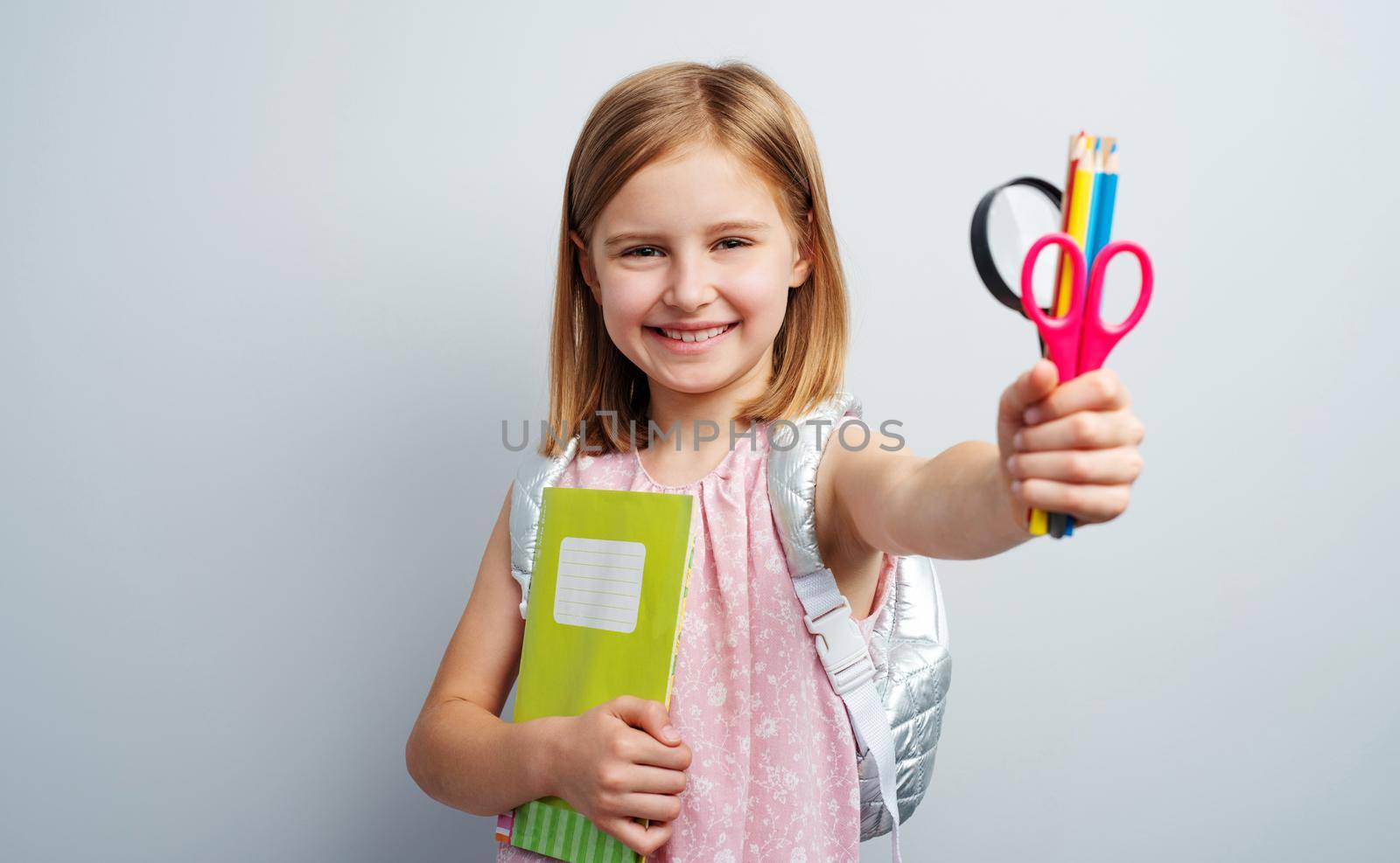 Portrait of schoolgirl with stationery supplies on gray wall background