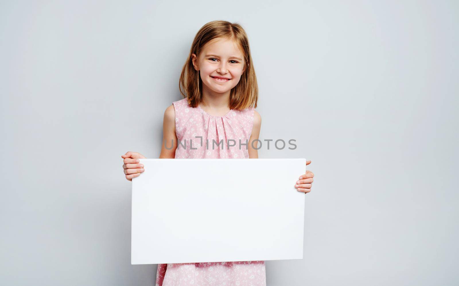 School girl holding horizontal blank white poster on a grey wall background