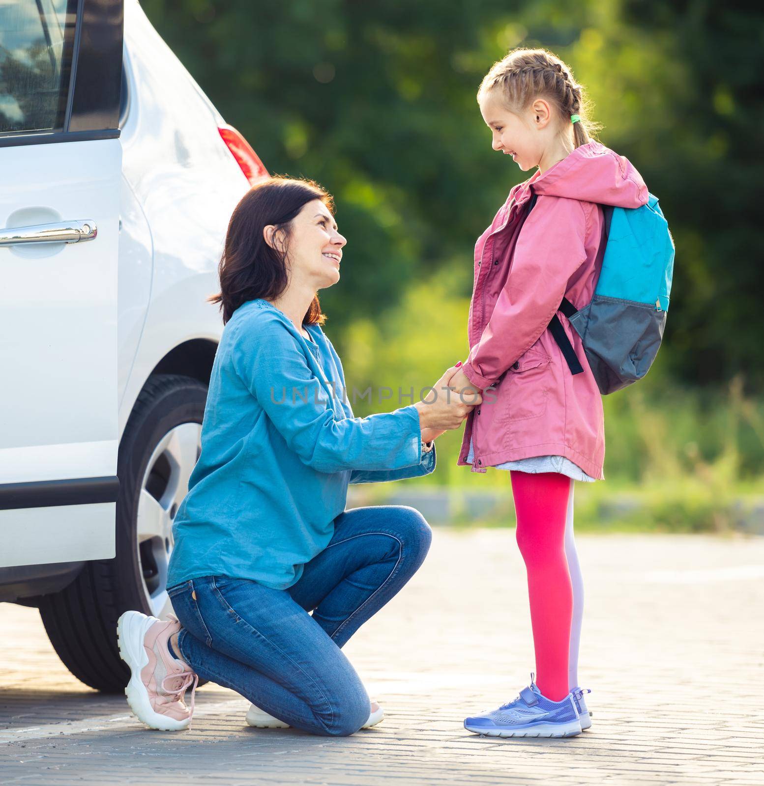 Smiling mother bringing daughter back to school saying goodbye on car parking