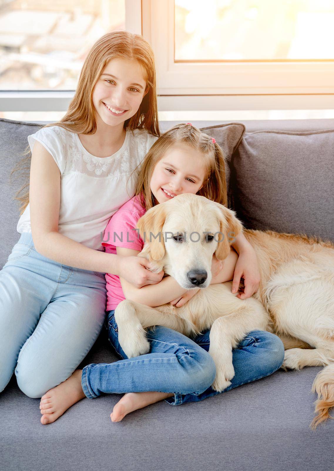 Happy sisters cuddling cute dog sitting on sofa at home