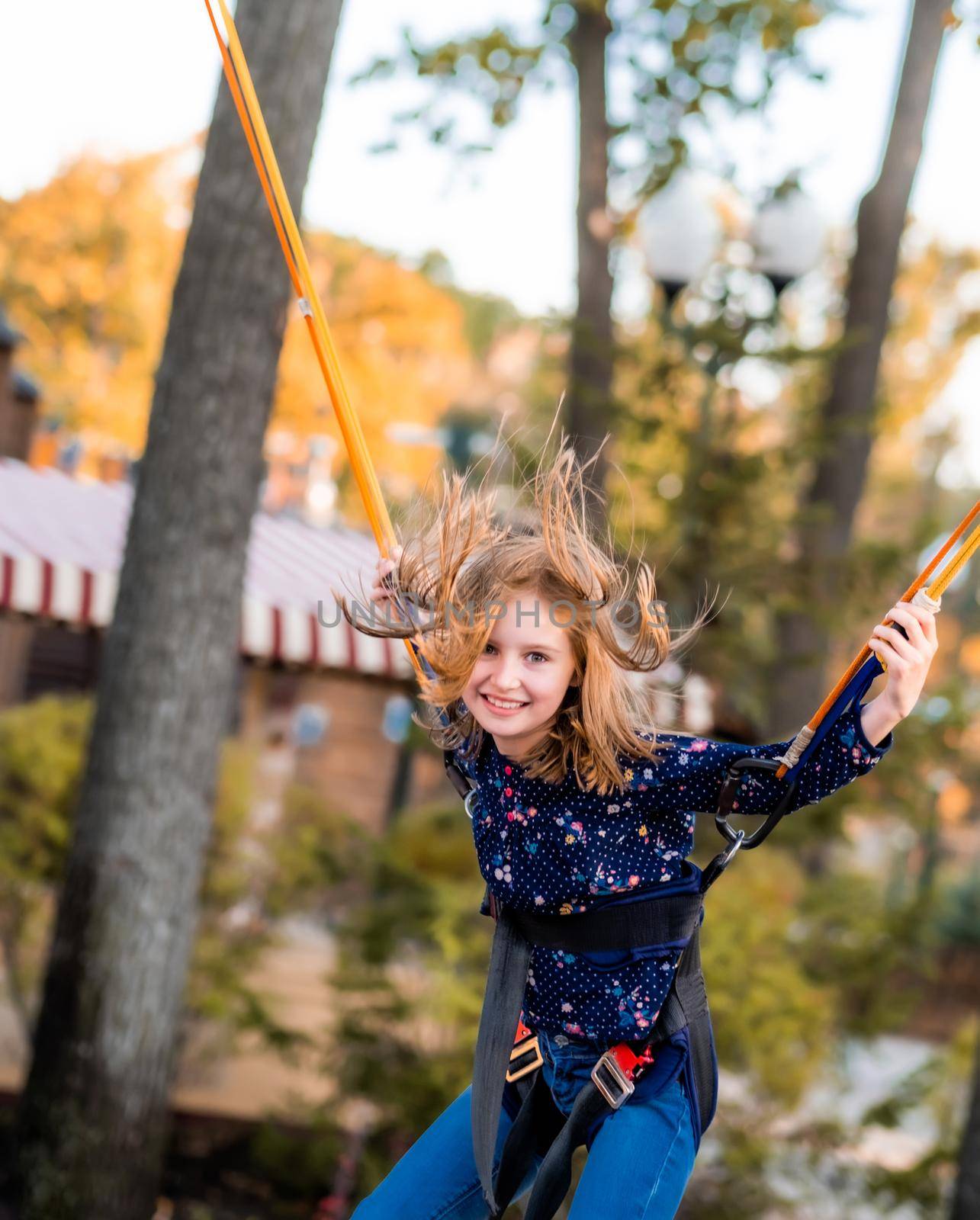 Smiling little girl jumping on trampoline jumping rope in autumn adventure park