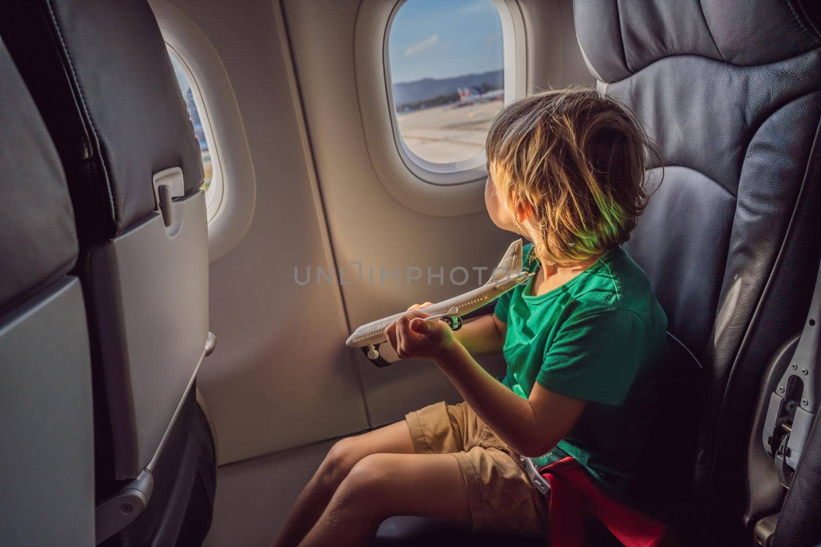 Little boy play with toy plane in the commercial jet airplane flying on vacation.