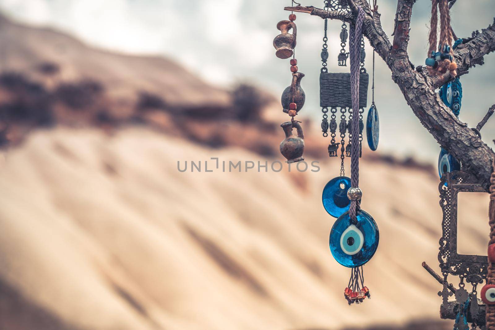Amulets against evil eye hanging on tree in front of sandy mountain in Cappadocia, Turkey