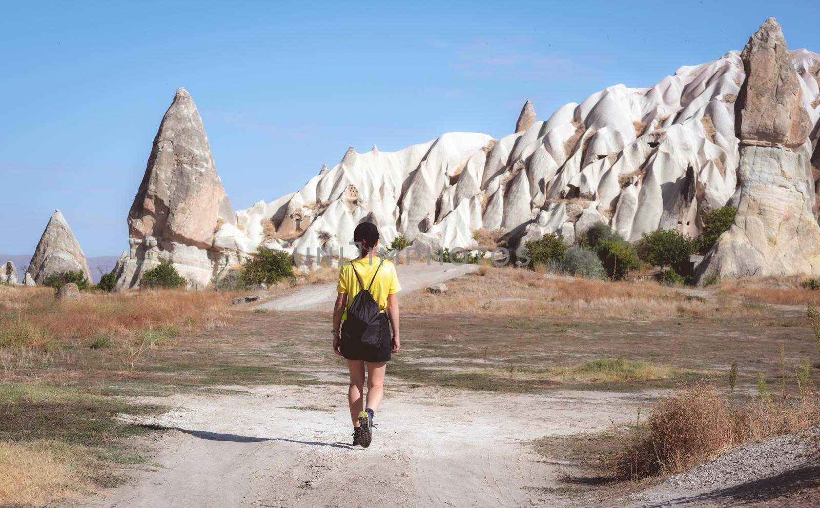 Rear view of woman tourist walking towards cave dwellings in Cappadocia, Turkey