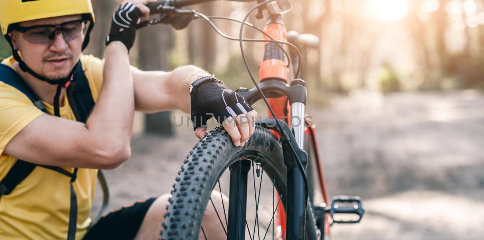 Cyclist checking front bicycle wheel pressure in sunny forest