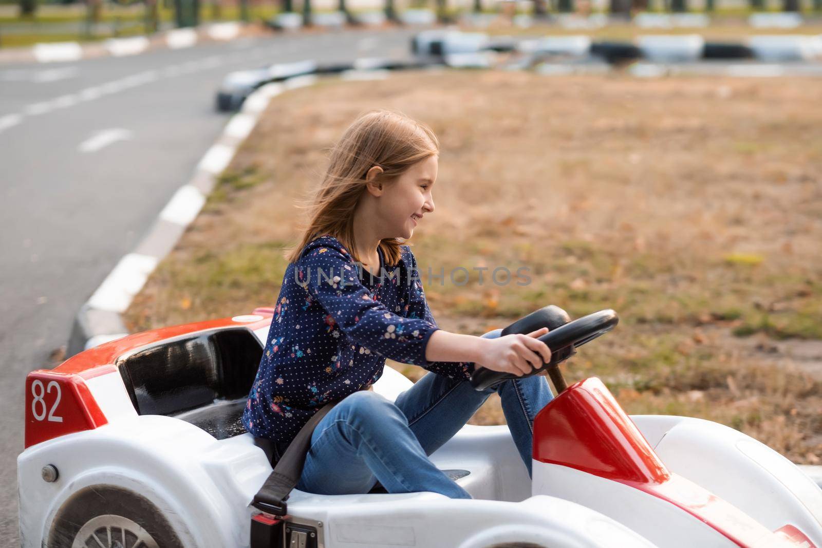 Happy little girl driving kart on track in autumn adventure park