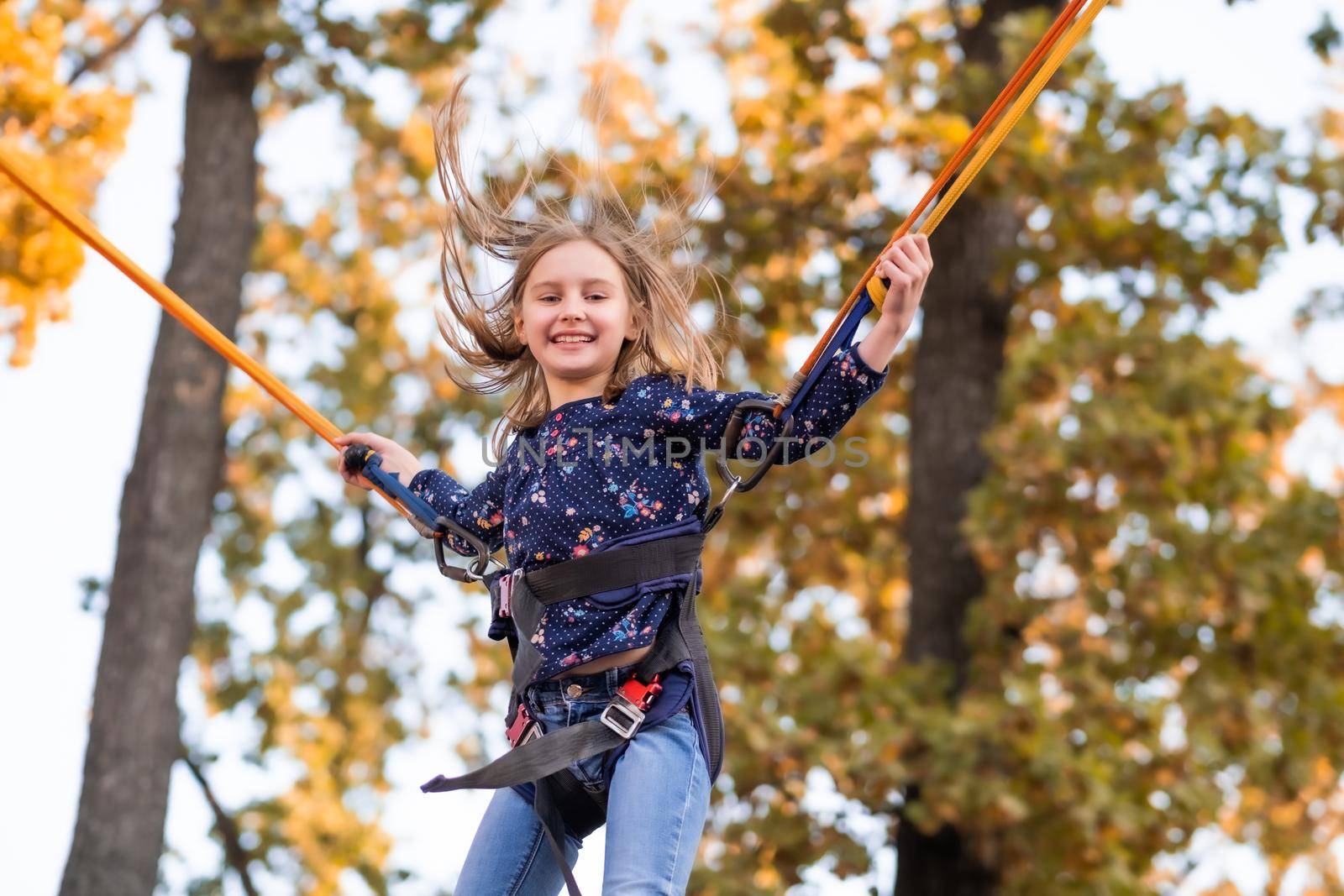 Happy little girl jupmping on trampoline ropes in adventure park