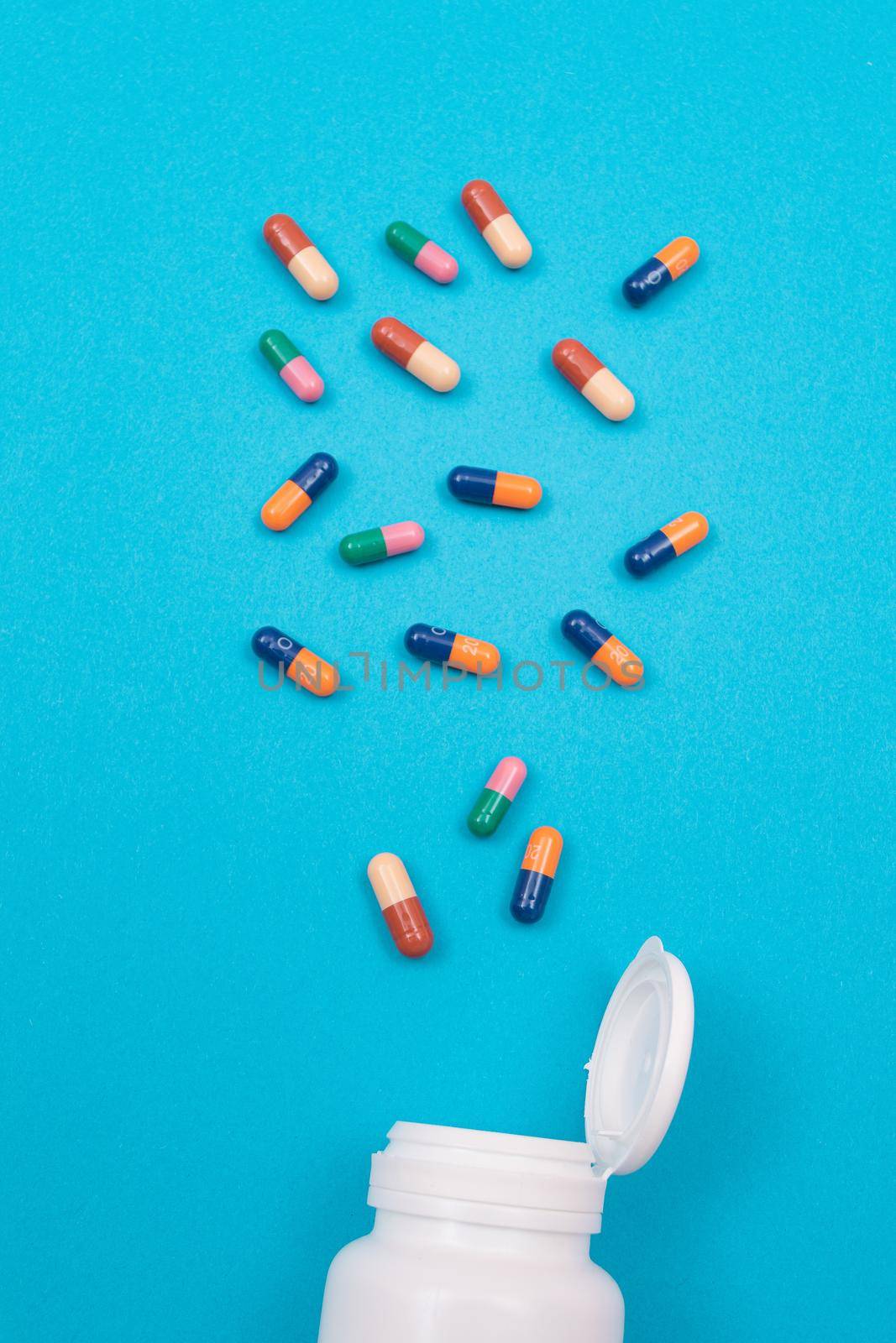 Global Pharmaceutical Industry and Medicinal Products - Colored Pills or Capsules Scattered from the Pill Container, Lying on Blue Background