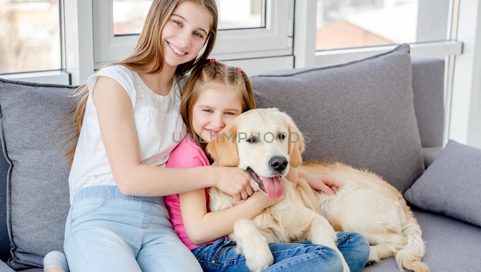 Smiling girls cuddling lovely dog in light room