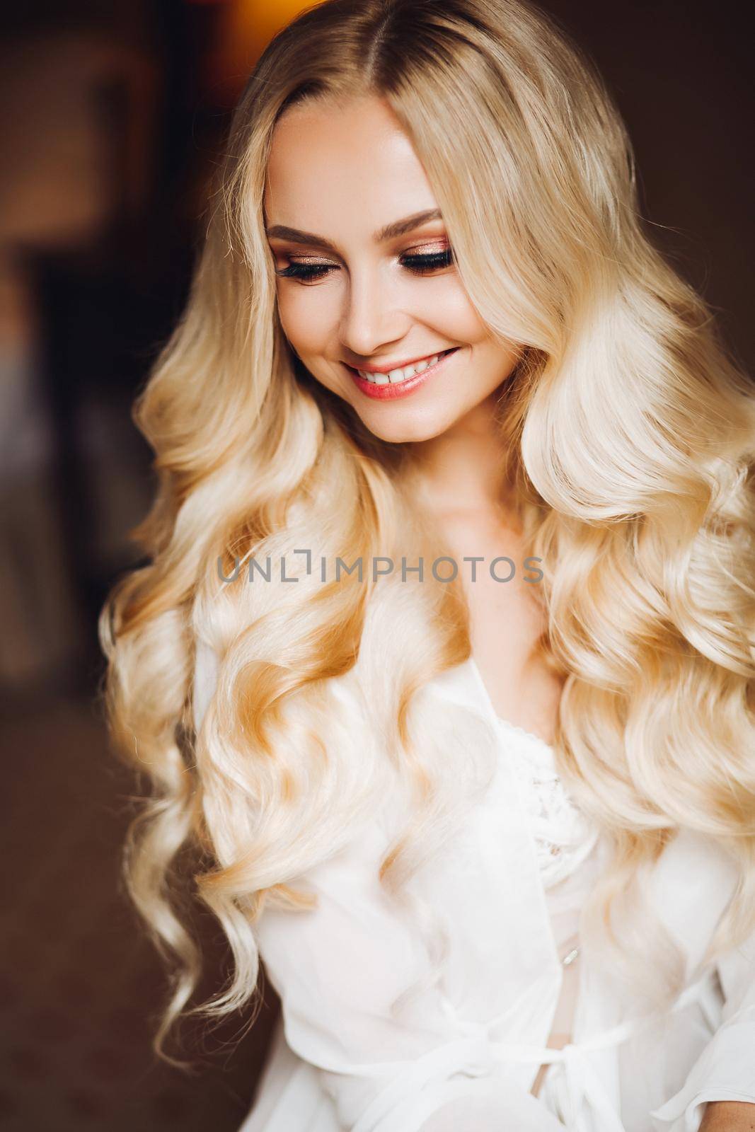 Portrait of gorgeous and sensuality blondie bride posing in bedroom, dreaming and smiling. Young, pretty woman with long curly hairwearing in white lace lingerie. Morning before wedding.