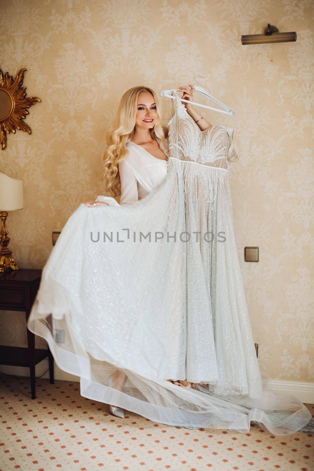 View of gorgeous woman standing near balcony and posing in white lace lingerie. Girl in vintage interior room, looking in big window. Bride at morning.