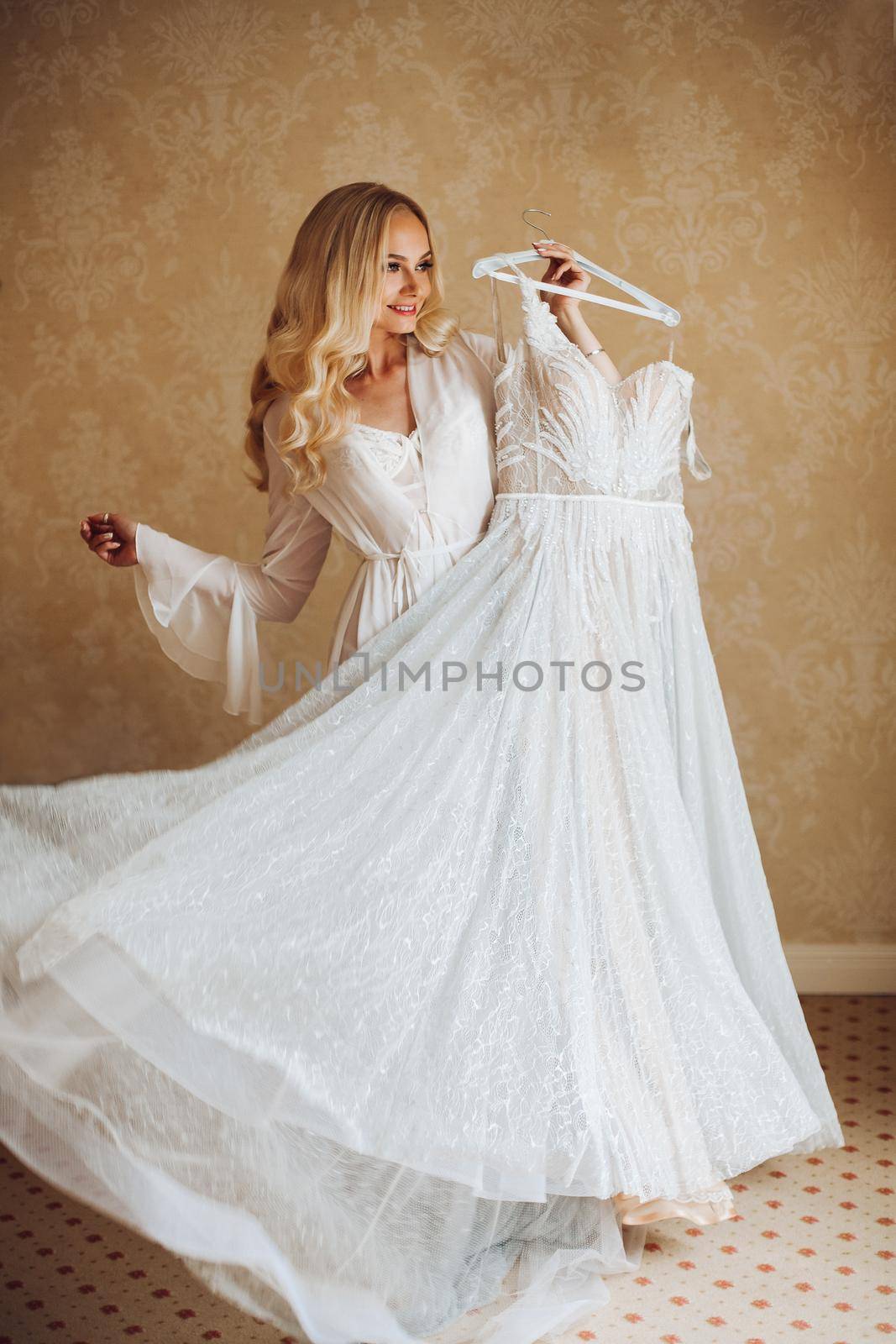 View of gorgeous woman standing near balcony and posing in white lace lingerie. Girl in vintage interior room, looking in big window. Bride at morning.
