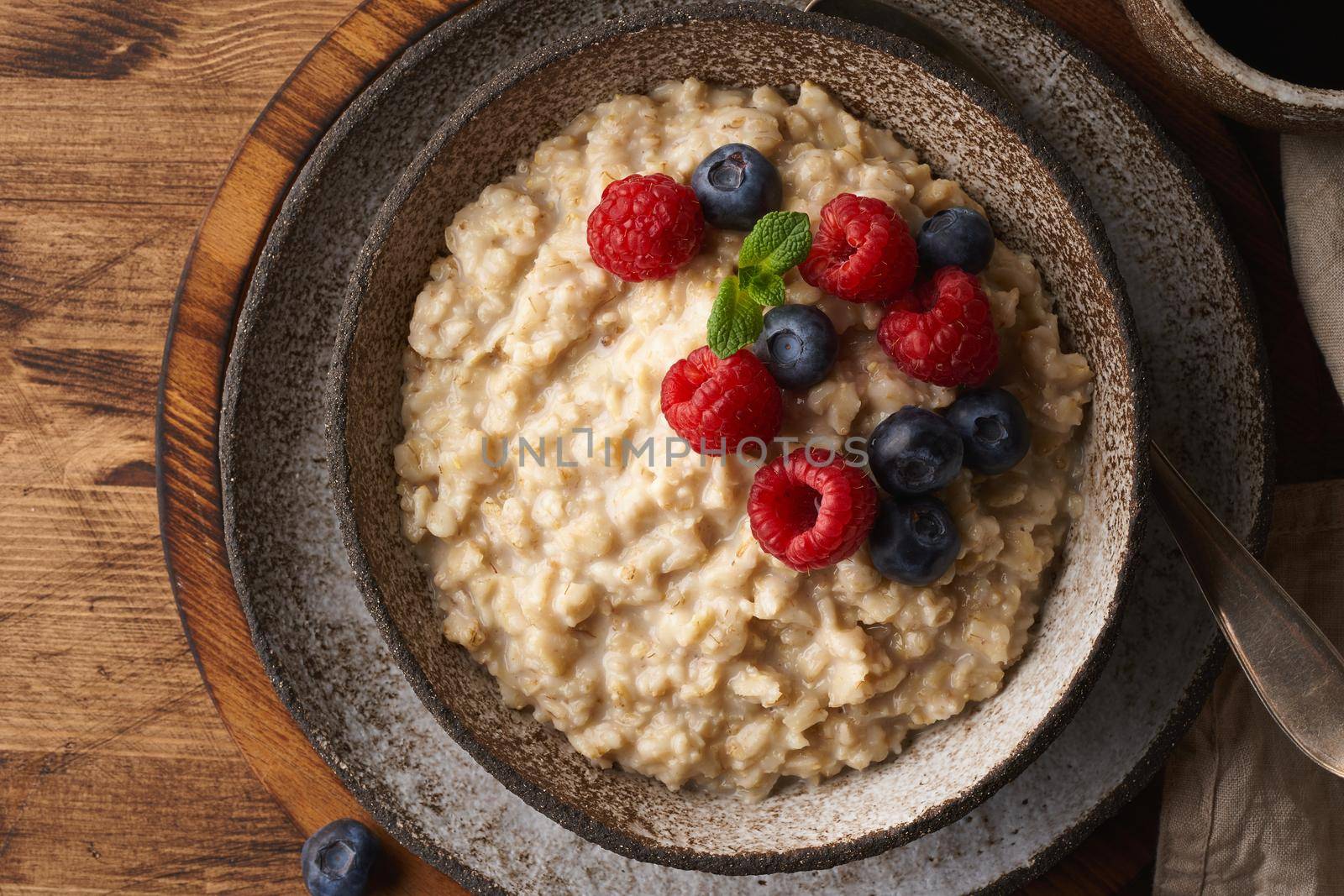 Oatmeal rustic porridge with blueberry, raspberries in ceramic vintage bowl, dash diet with berries, wooden dark brown background, top view close up. Healthy diet breakfast