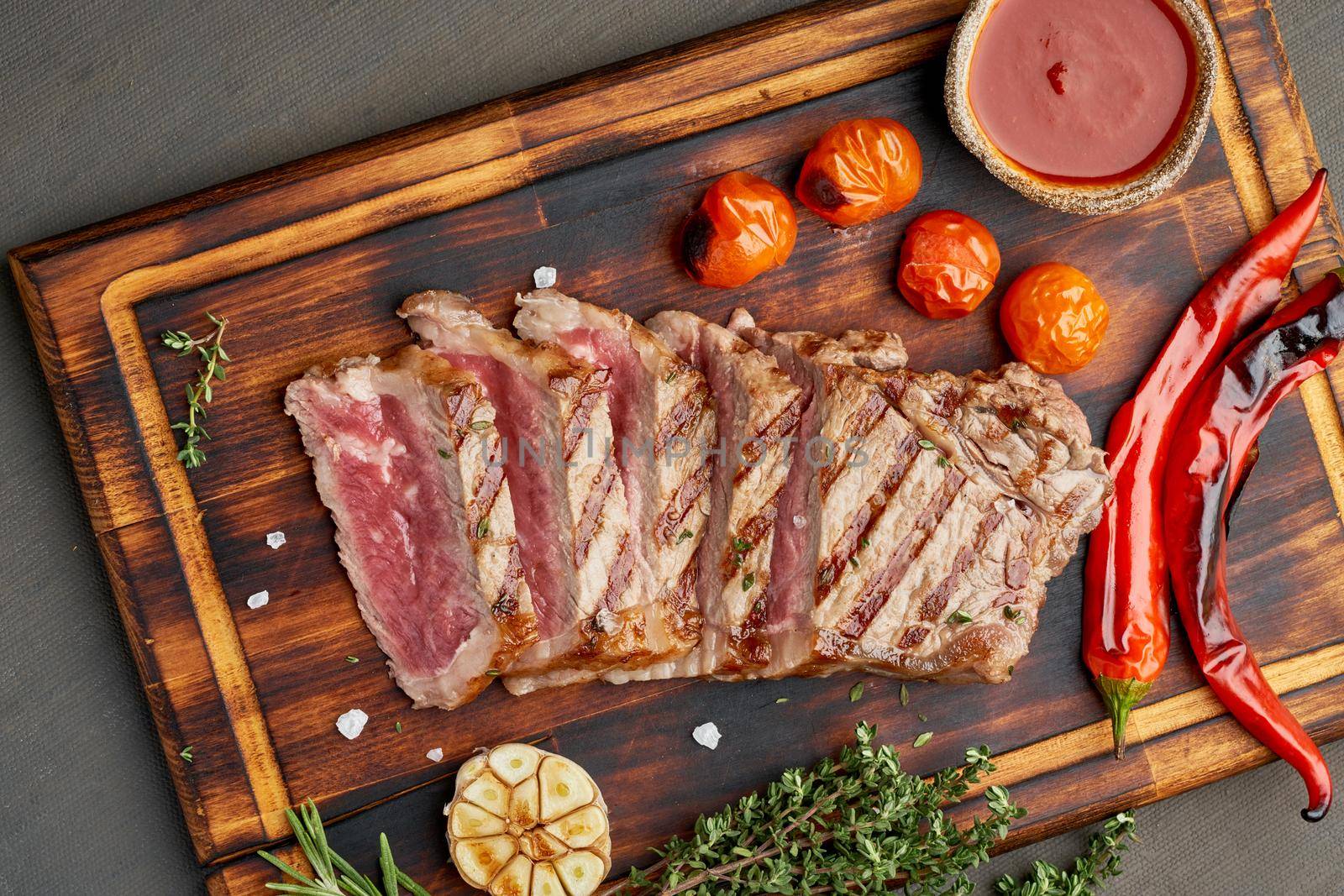 Keto ketogenic diet grilled fried beef steak, striploin on cutting board on dark brown table. Paleo food recipe with grilled fried chopped piece of meat, papper, top view