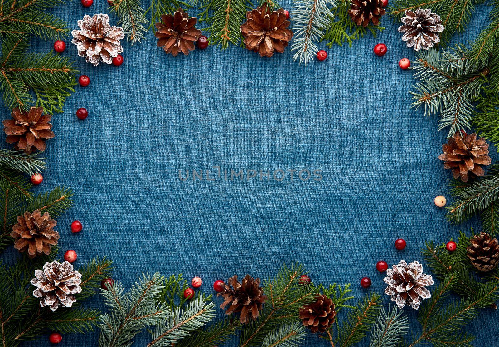 Christmas and Happy New Year dark blue background. Frame with fir branches, cones, cranberry berries. Textile backdrop with copy space.