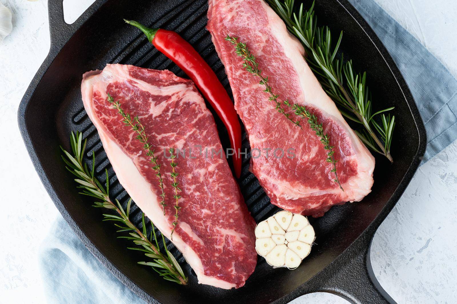 Two fresh raw big whole pieces of meat, beef fillet, marble striploin in cast-iron large pan. Top view, close up. Seasoning steak with salt.