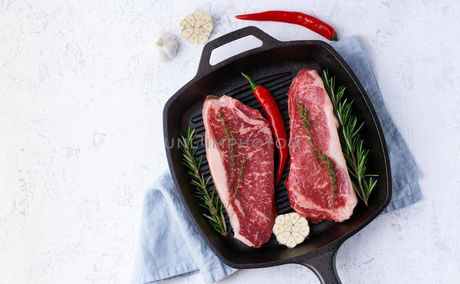 Two fresh raw big whole pieces of meat, beef fillet, marble striploin in cast-iron large pan. Top view. Seasoning steak with salt.