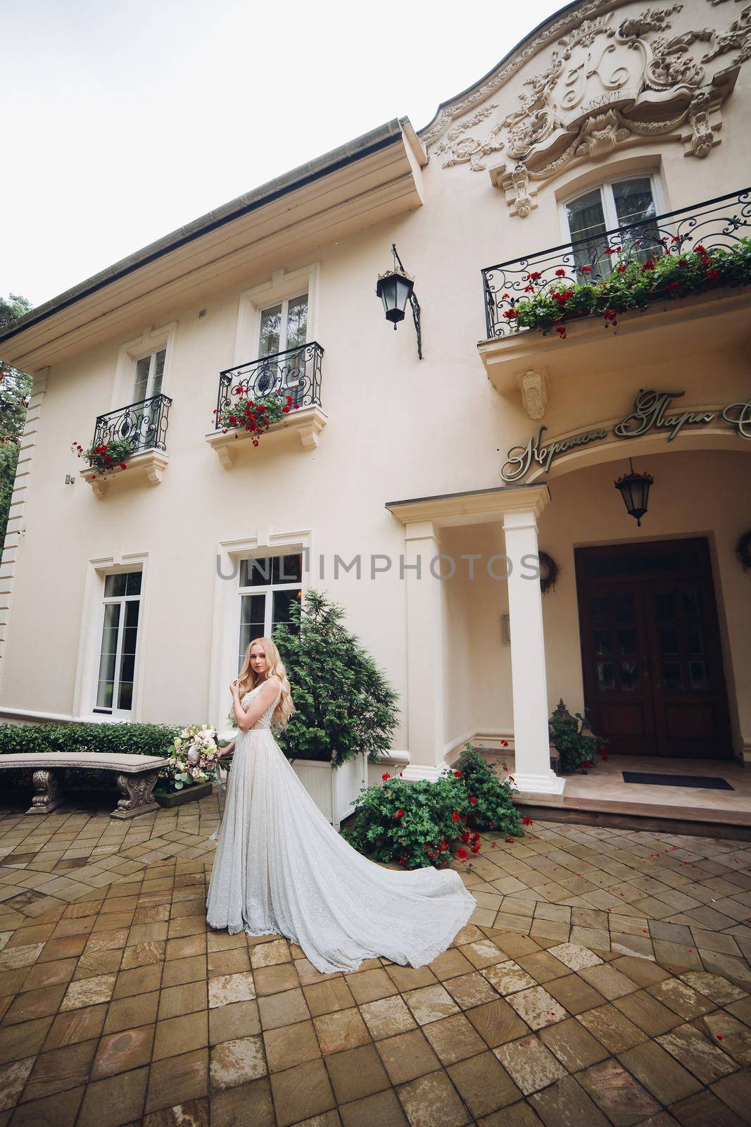 Bride in perfect wedding dress posing against luxury house with wedding boquet. by StudioLucky