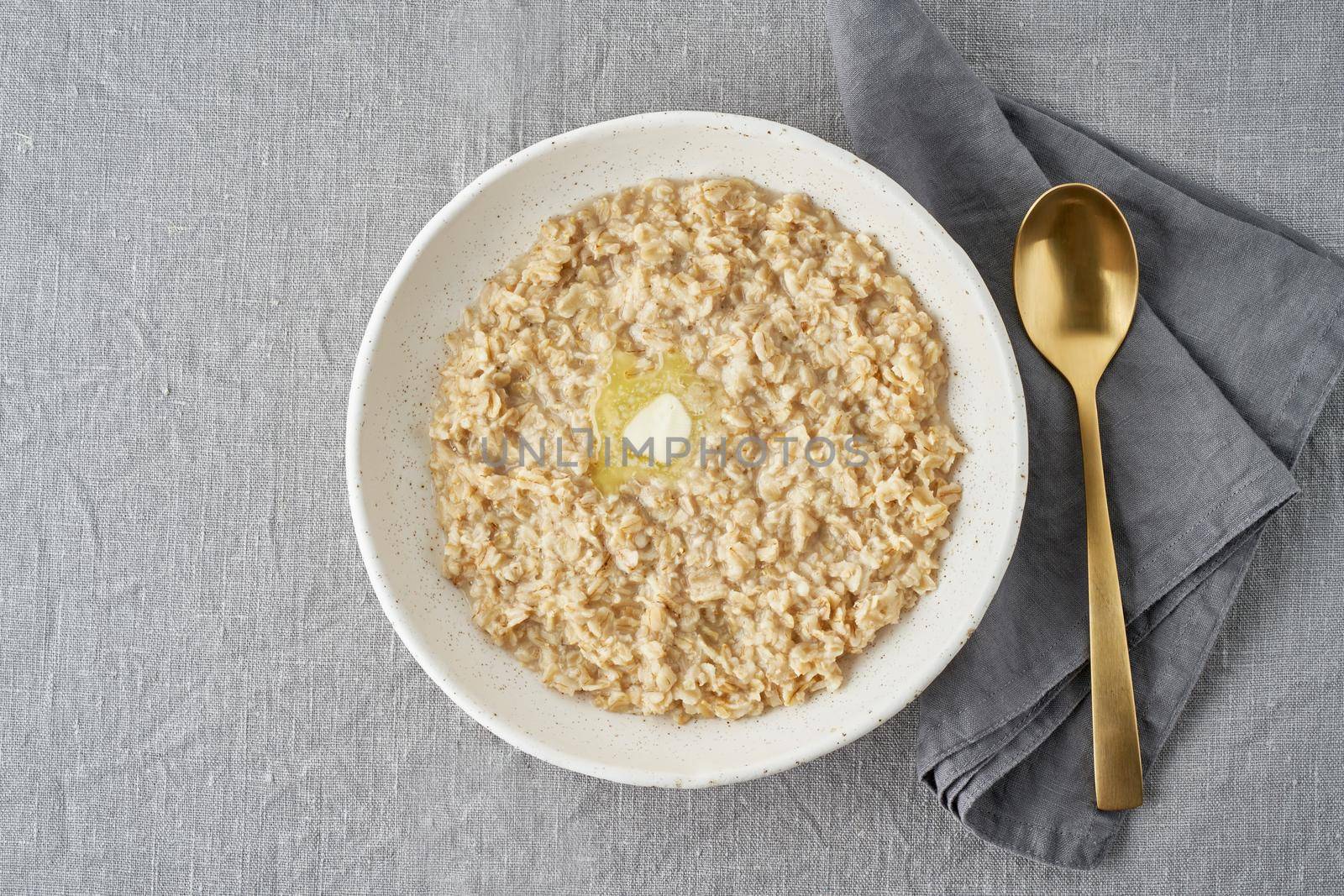 Whole oatmeal, large bowl of porridge with butter for breakfast, morning meal. Top view, close up, gray table. Vegan tasty healthy diet. Copy space