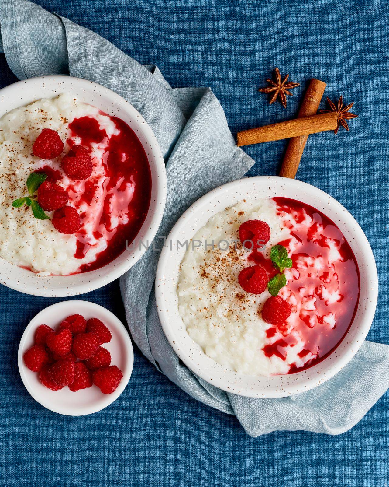 Rice pudding. French milk rice dessert with raspberries, blueberries, berries, jam. Healthy Vegan diet breakfast with coconut milk, cinnamon. Blue linen textile. Top view, vertical