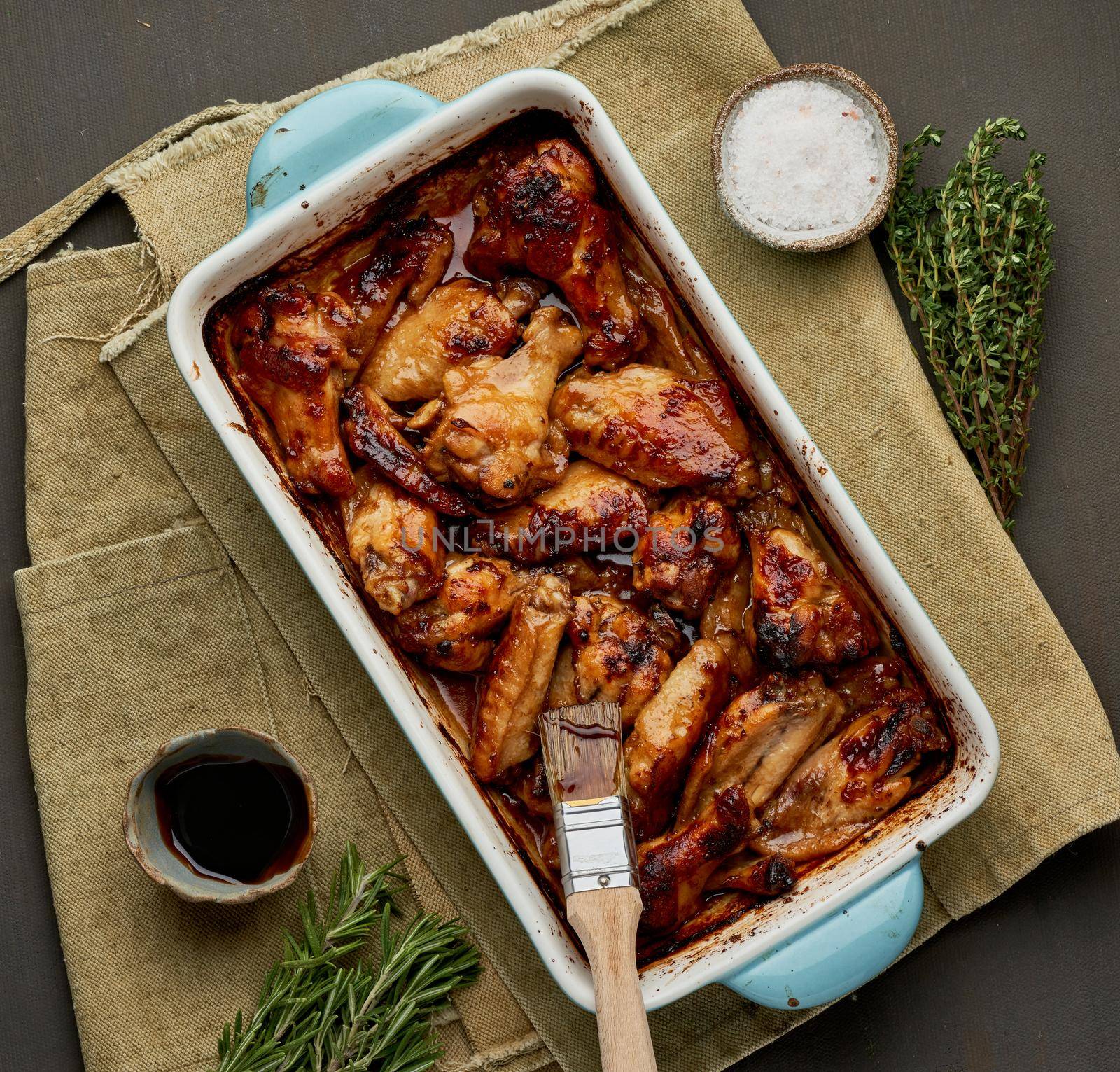 Barbecue chicken wings. Slow cooker sweet and spicy. Oven baked marinated chiken in blue ceramic tray with brush in bbq red sauce. Dark rustic table. Top view, close up