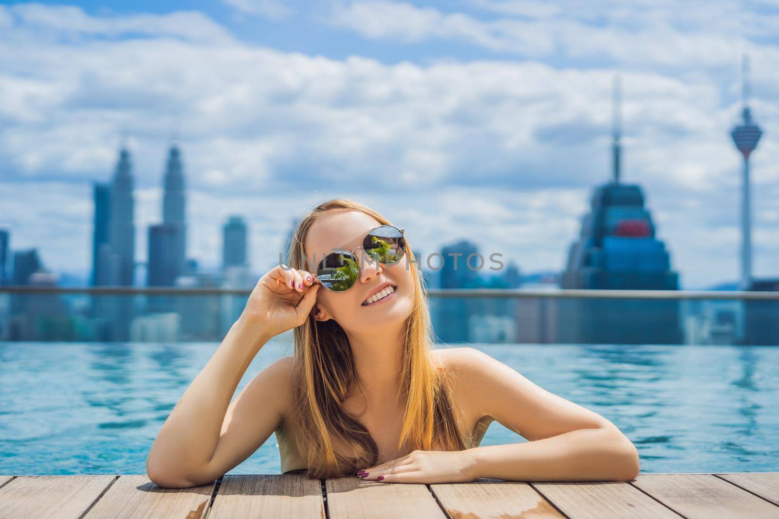 Young woman in outdoor swimming pool with city view in blue sky.