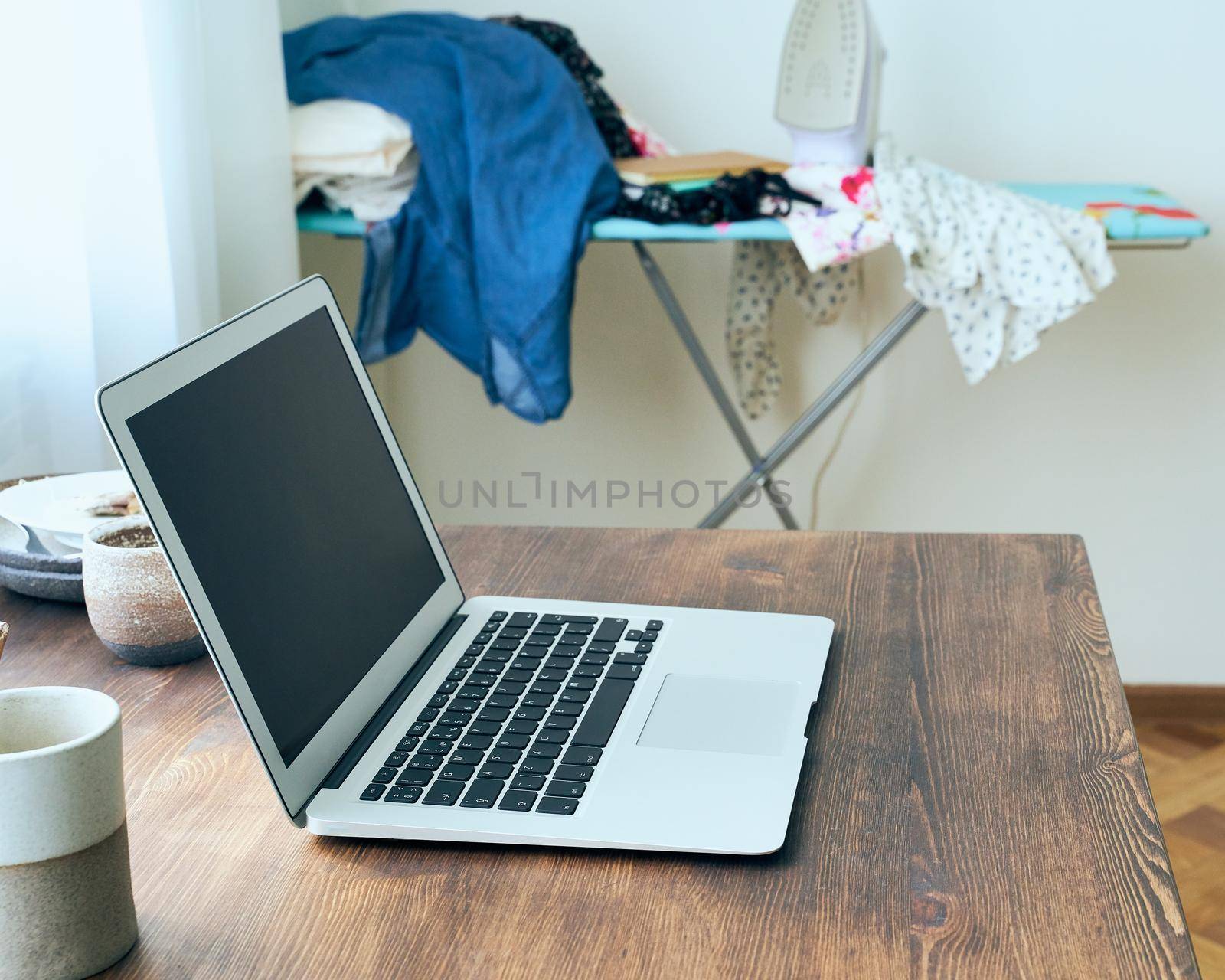 Freelance Desk with laptop in mess at home apartment. Quarantine, self-isolation, sociophobia. Online learning, teleworking, online lectures. Concept of digital nomads, home office