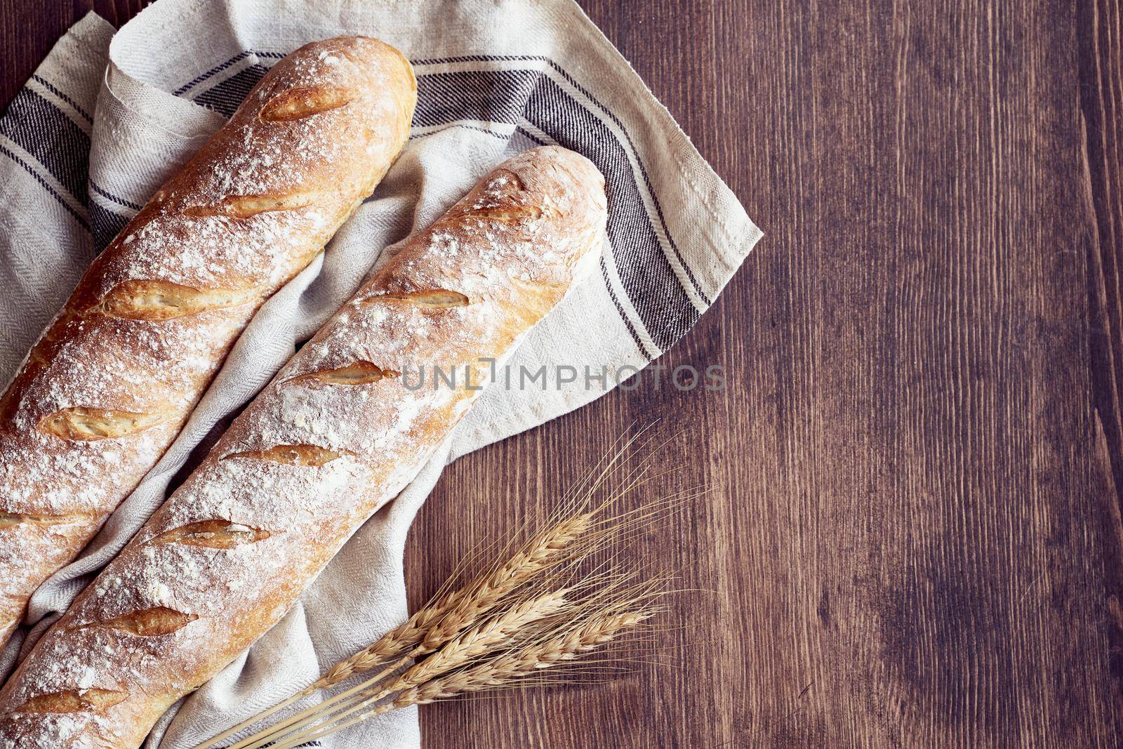 Fresh baked homemade crusty bread baguette. Two loaves on linen towel on wooden table. Delicious and healthy homemade cakes. Copy space