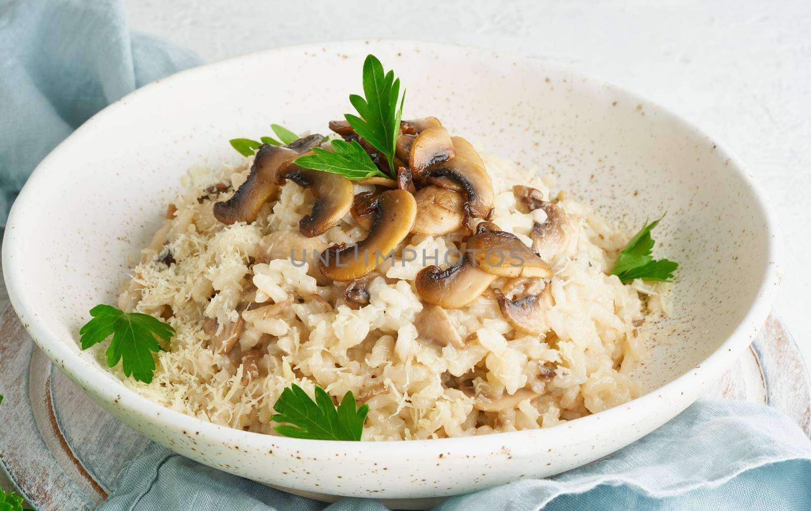 Risotto with mushrooms in plate. Rice porridge with mushrooms and parsley. White table, spoons, mushrooms. Hot dish, italian cuisine, side view
