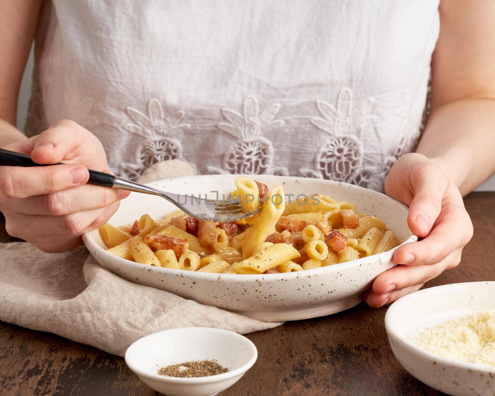 Carbonara pasta. Woman sits at table and eats pasta penne with pancetta, by NataBene