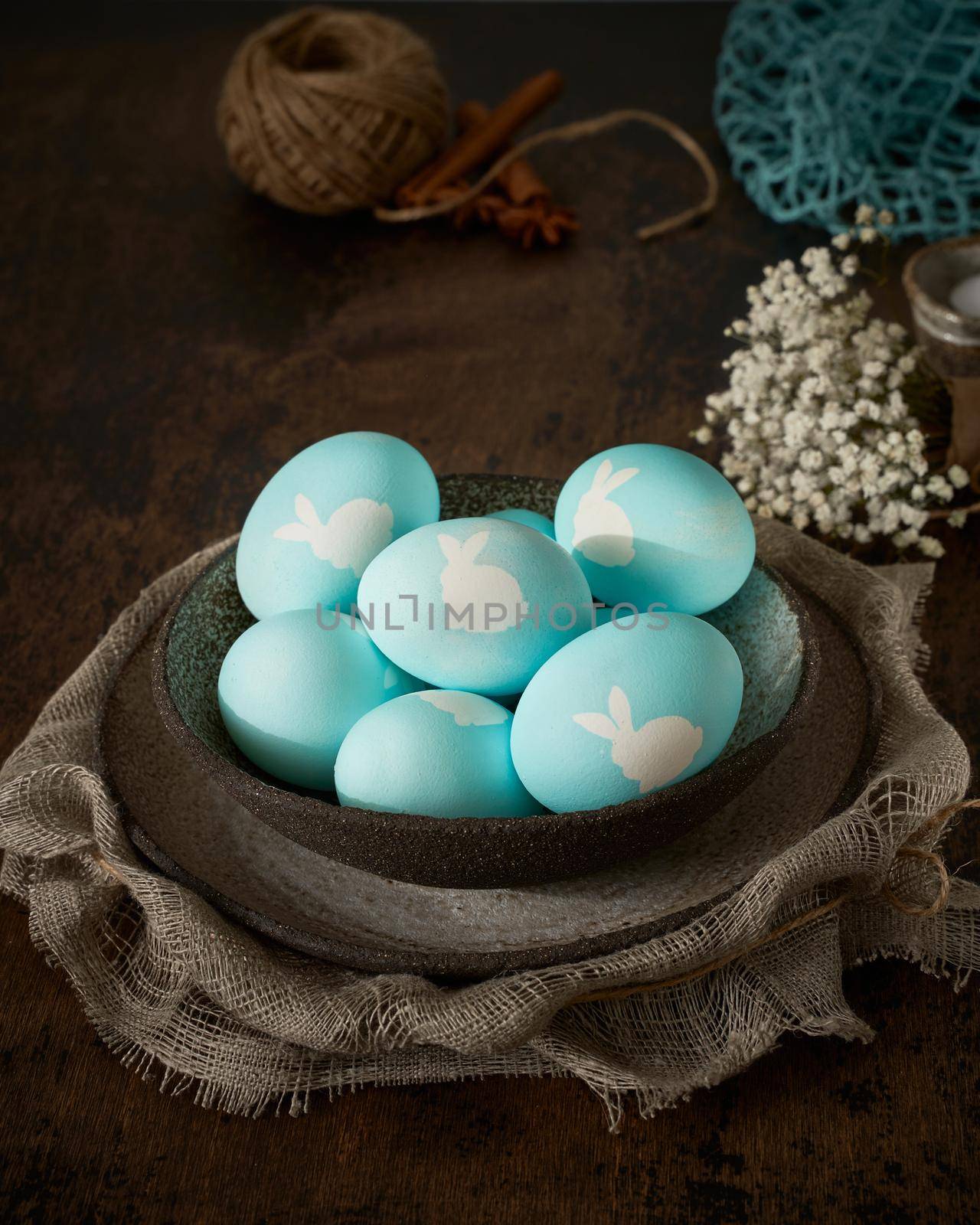 Unusual Easter on dark old background. Ceramic brown bowl with blue eggs. Darkness, rays of sunlight shine on eggs. Concept of new life, rebirth. Rustic style. Vertical, copy space