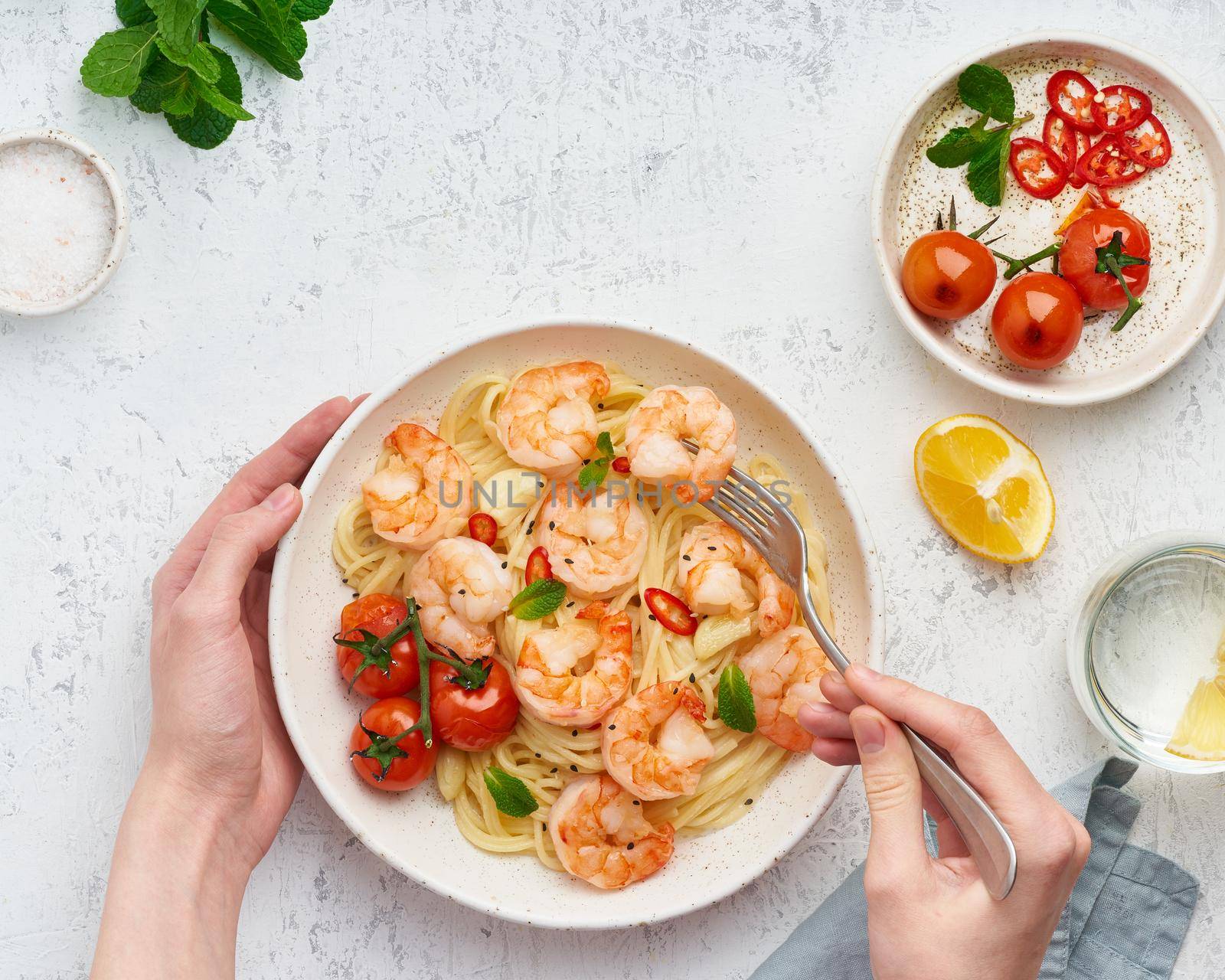 Pasta bavette with fried shrimps, bechamel sauce. Woman hands in frame, girl eats pasta, holds fork in hands, top view, italian cuisine.