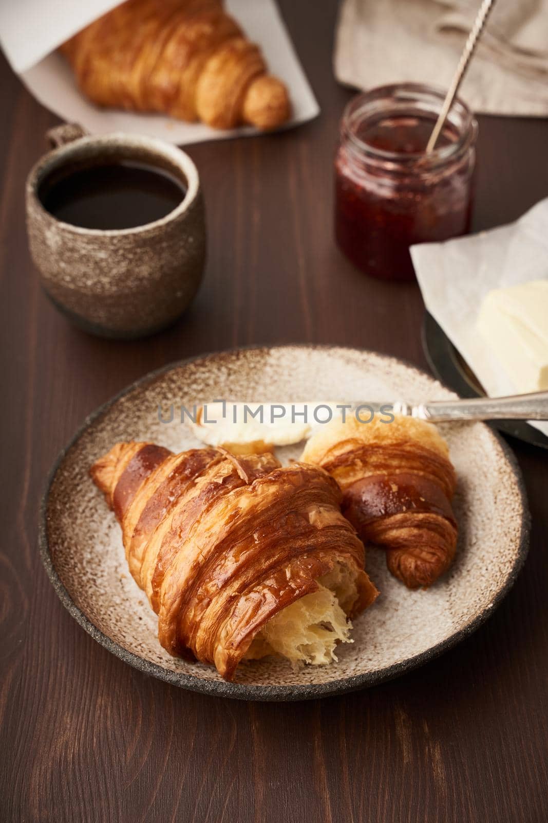 Morning breakfast with croissant on plate, cup of coffee, jam and butter. Vertical, side view by NataBene