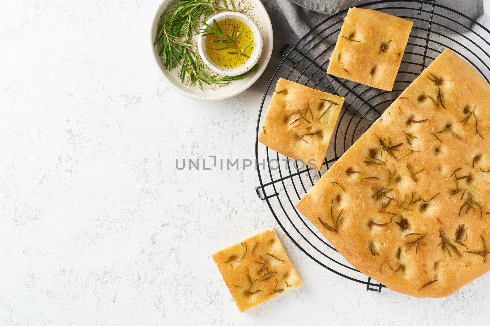 Focaccia, pizza, italian flat bread with rosemary and olive oil on grid on white rustic table, tradition italian cuisine, top view, copy space