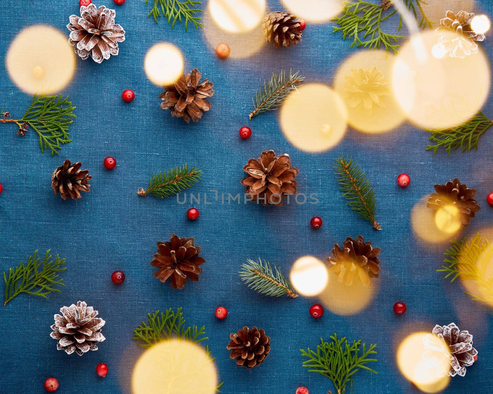 Christmas and Happy New Year dark blue background. Pattern with golden light glow garland bokeh and fir branches, cones, cranberry berries. Textile backdrop with copy space.