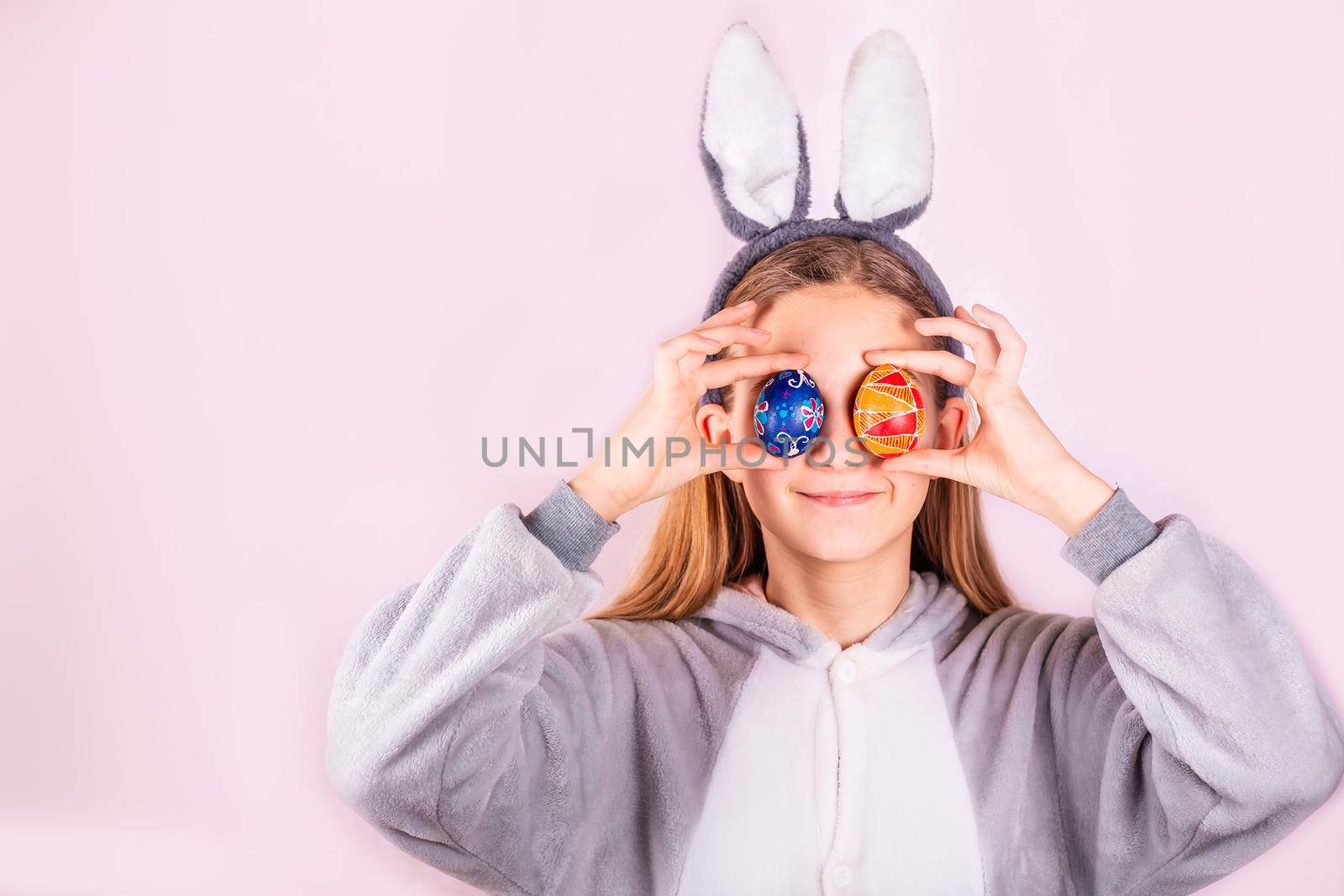 Girl in rabbit bunny ears on head with colored eggs on pink background. Cheerful smiling happy child. Easter holiday banner