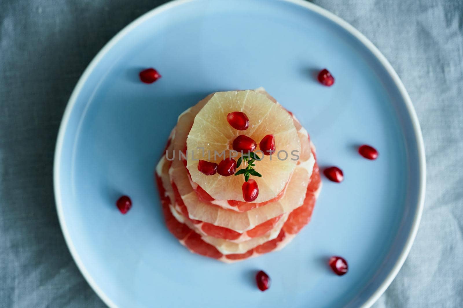 Top view stack of sliced round slices of red and white grapefruit sprinkled with pomegranate seeds on blue plate. Bright mix of citrus fruits