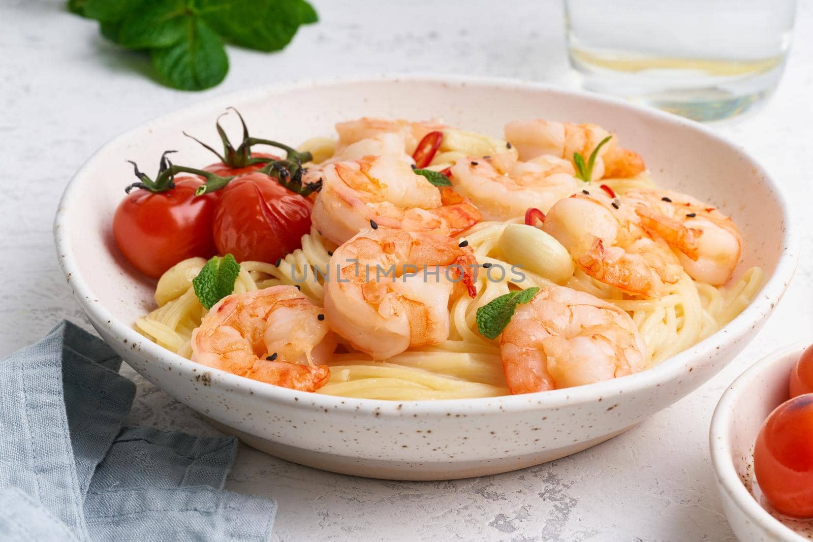 Seafood pasta spaghetti with fried shrimps, bechamel sauce, mint leaf and tomatoes on white table by NataBene