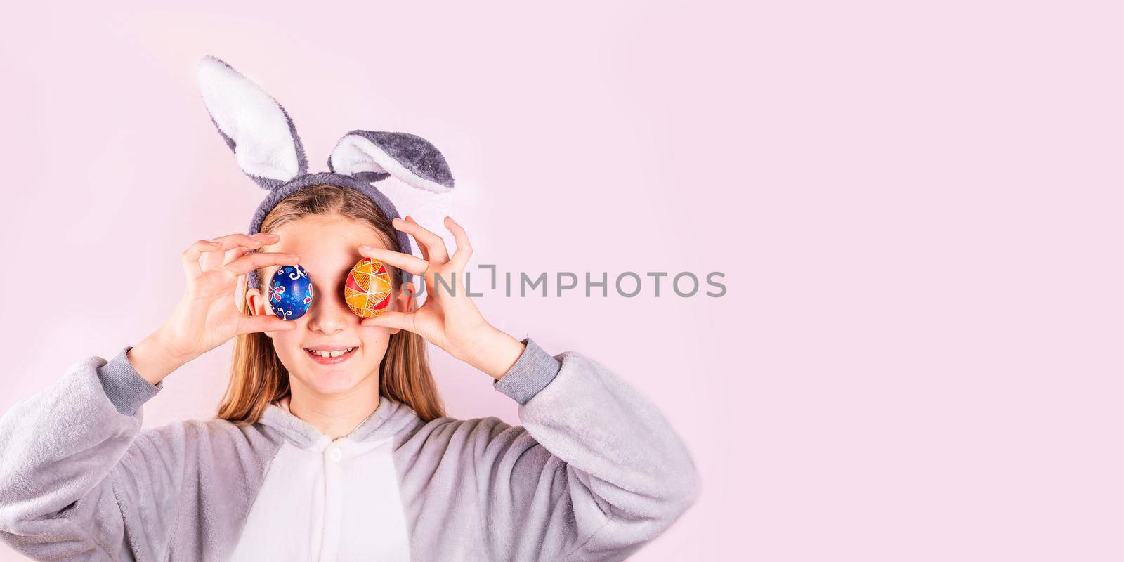 Girl in rabbit bunny ears on head with colored eggs on pink background. Cheerful smiling happy child. Easter holiday banner