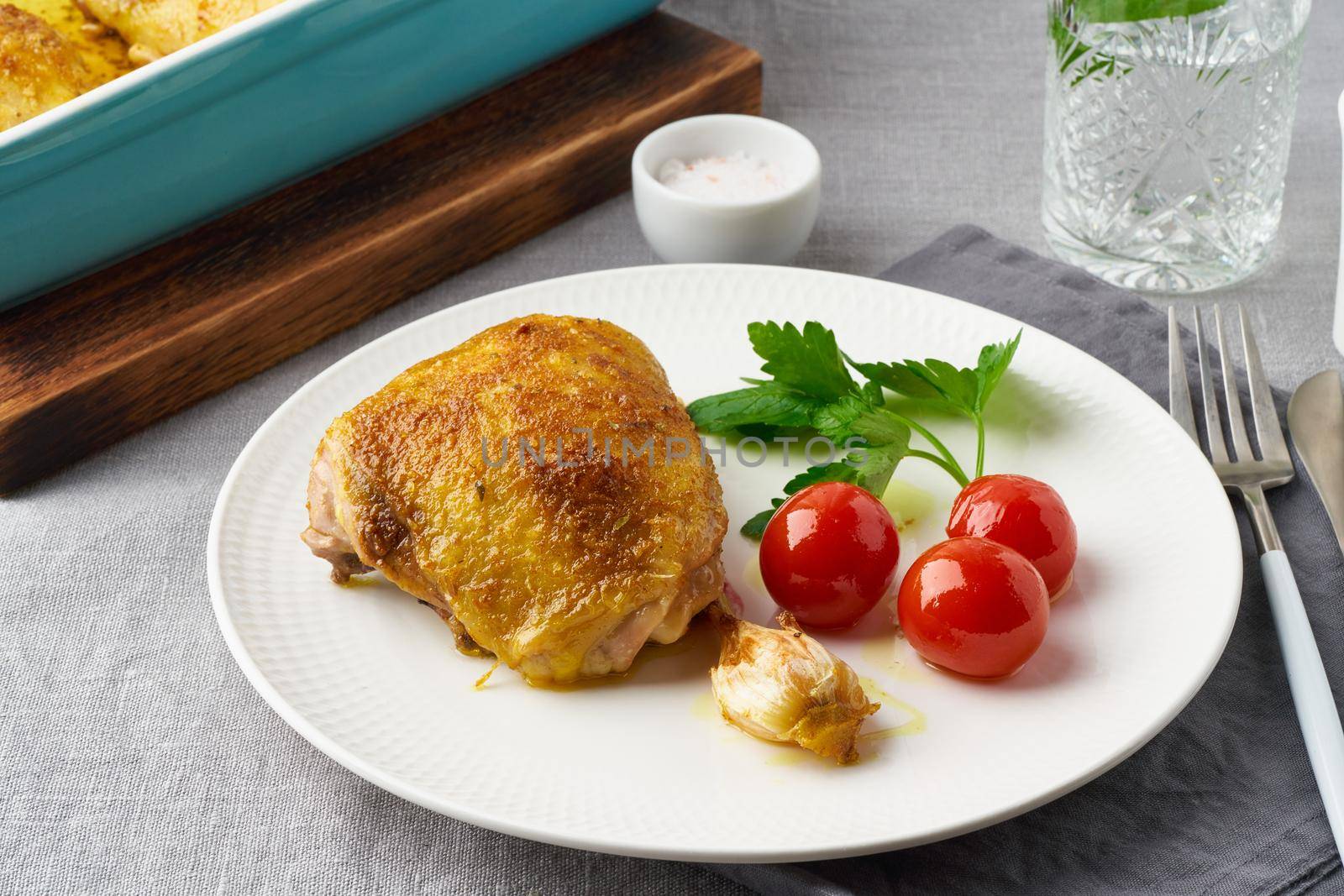 Chicken thighs baked with turmeric, tomatoes and garlic. Fried chicken is on plate, gray tablecloth, tray of meat. Healthy diet, clean eating, paleo, keto, ketogenic